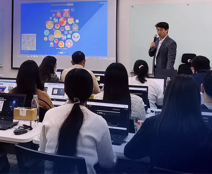 วิทยากรชายสวมสูทสีเทาถือไมค์บรรยายในห้องเรียน GenAI for Business